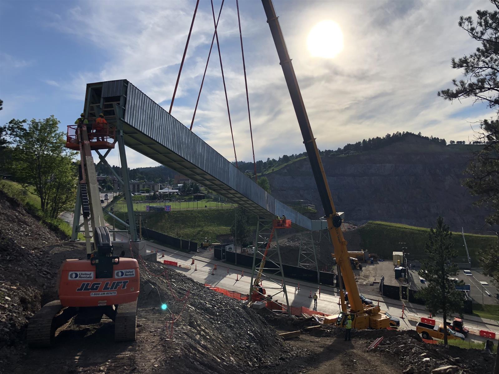 A crane holds a segment of the conveyor in place over the highway