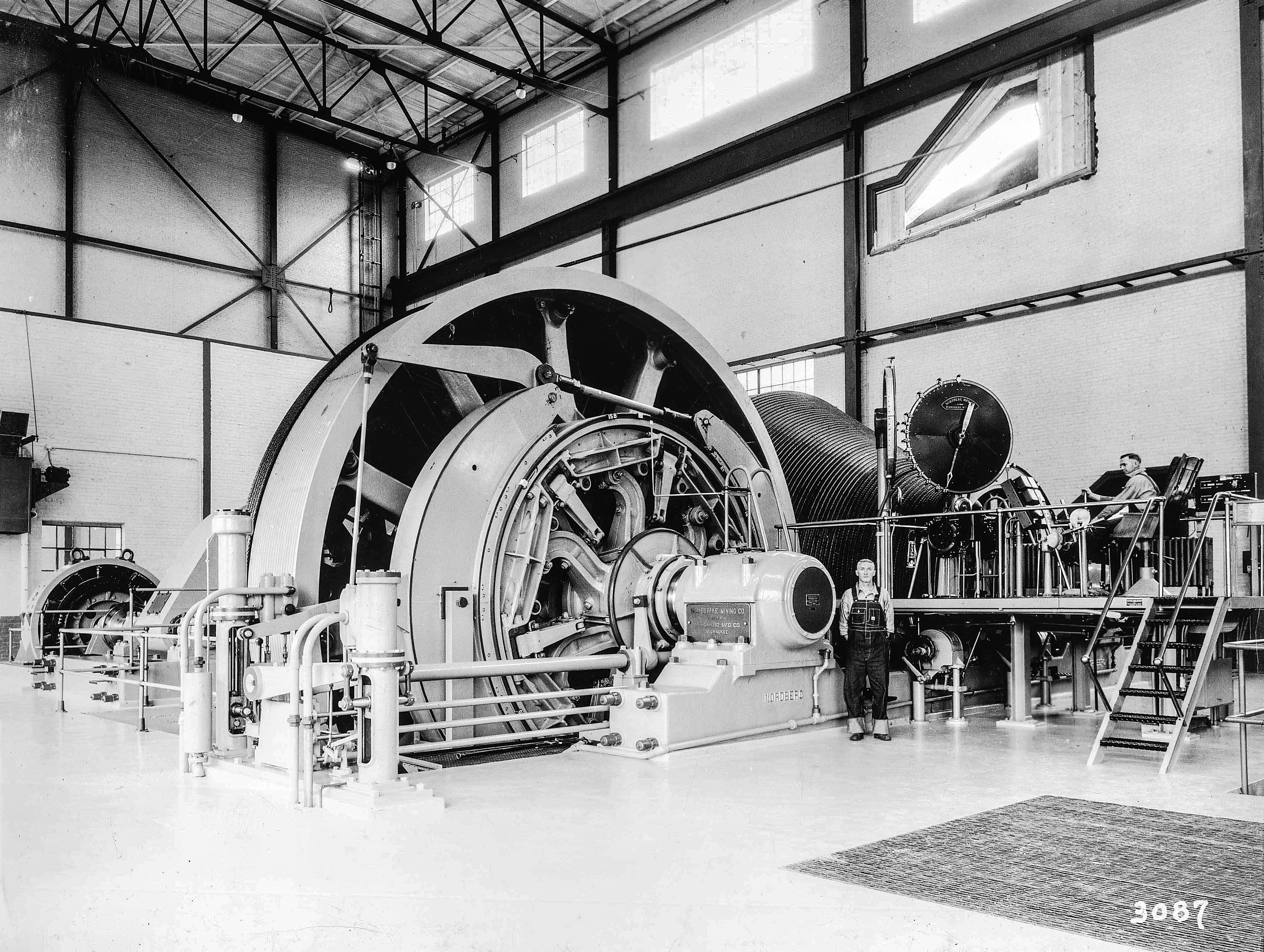 a black and white photo of a young man standing in front of the Ross Production hoist