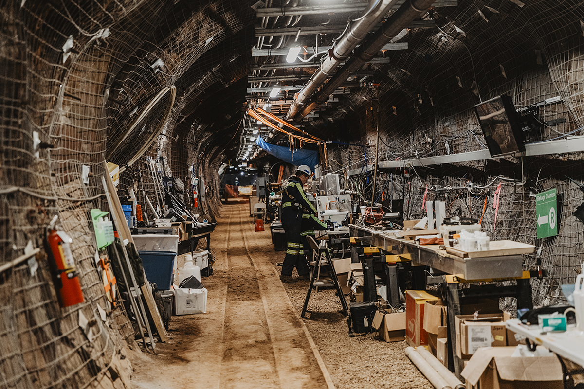 A researcher stands in an underground drift. The drift is outfitted with geothermal energy research instrumentation.