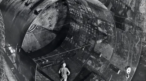 In a black and white photo, a man stands in a large, underground tank.